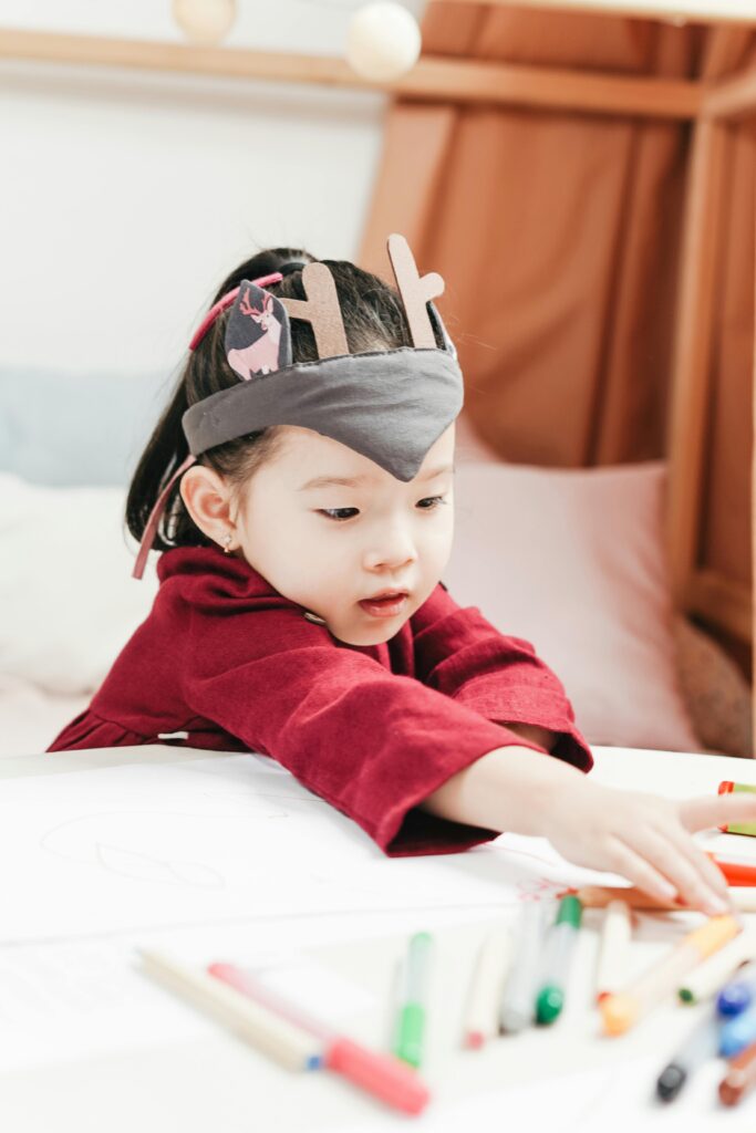 Cute child playing with crayons indoors, showcasing creativity and innocence.