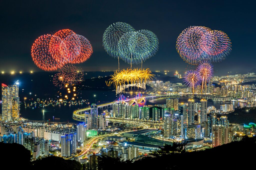 Vibrant fireworks illuminate the night sky over Busan, showcasing the city's stunning skyline and bridges.