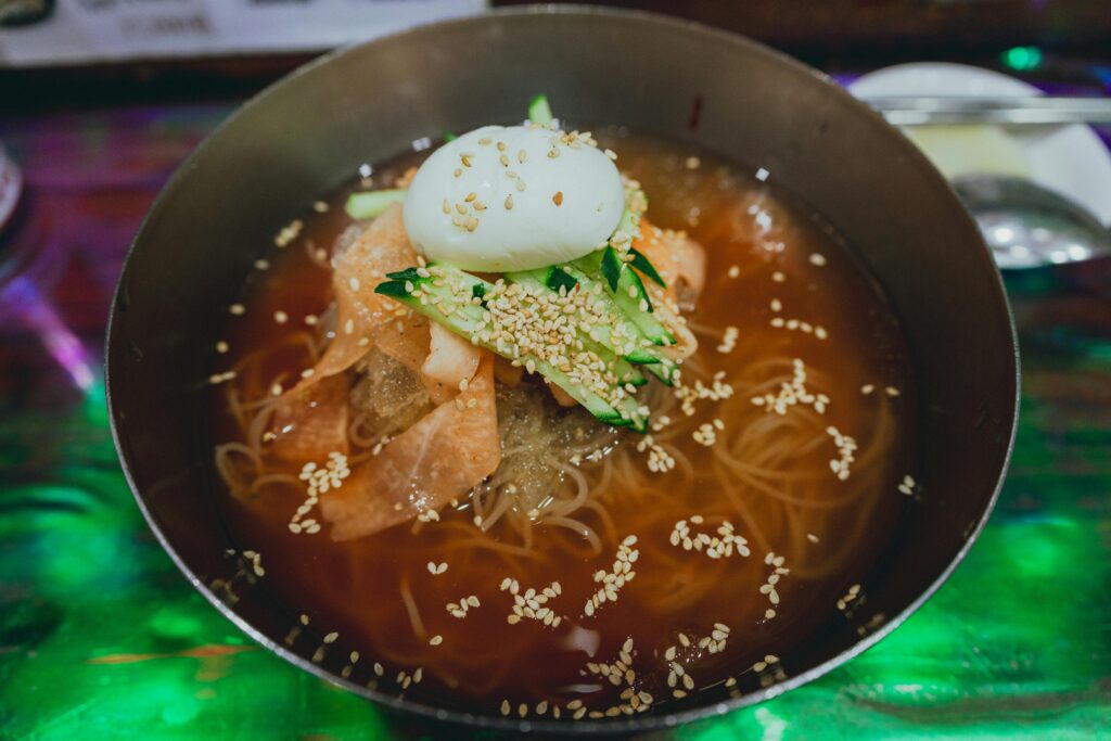 Delicious Korean cold noodles (Mul Naengmyeon) garnished with egg, cucumber, and sesame seeds.