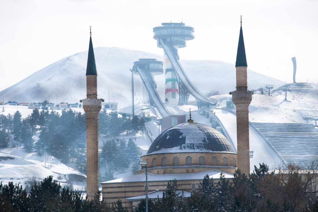 A snowy view of the mosque in Erzurum, Türkiye, with ski jumps in the backdrop, capturing winter's serene beauty.